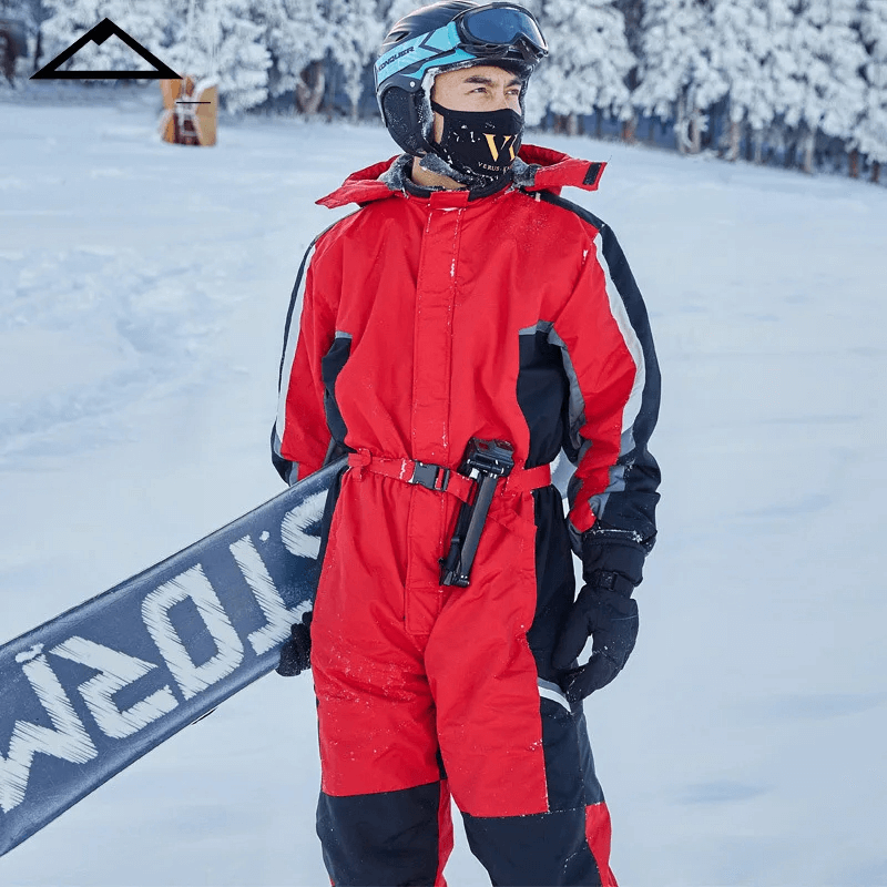 Man wearing red ski jumpsuit with fleece lining, carrying snowboard in snowy landscape. Waterproof, windproof, and warm for winter sports.